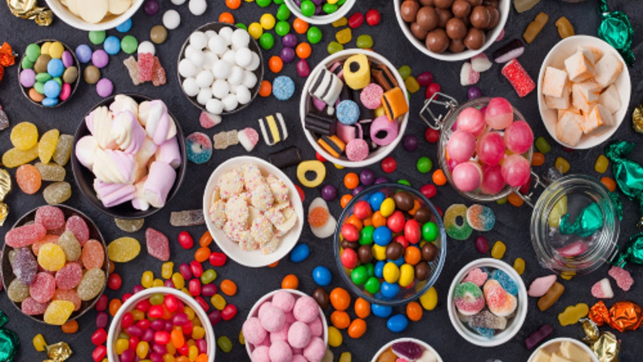 Pink lollipop candies in jar with various milk chocolate and jelly gums candies on black with liquorice allsorts and strawberry bonbons and large variety of sweets and candies.