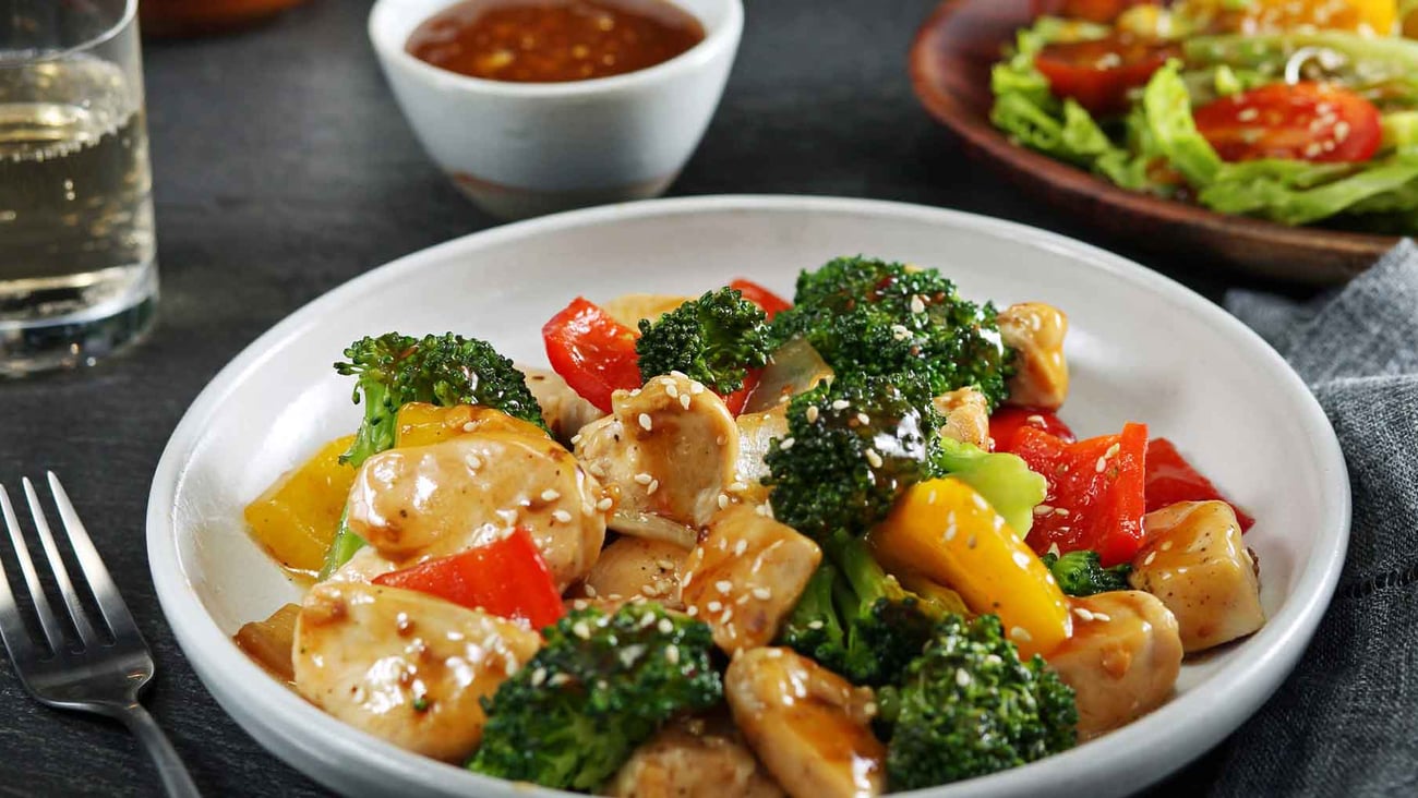 Sesame stirfry plated with chicken and broccoli on nicely set table