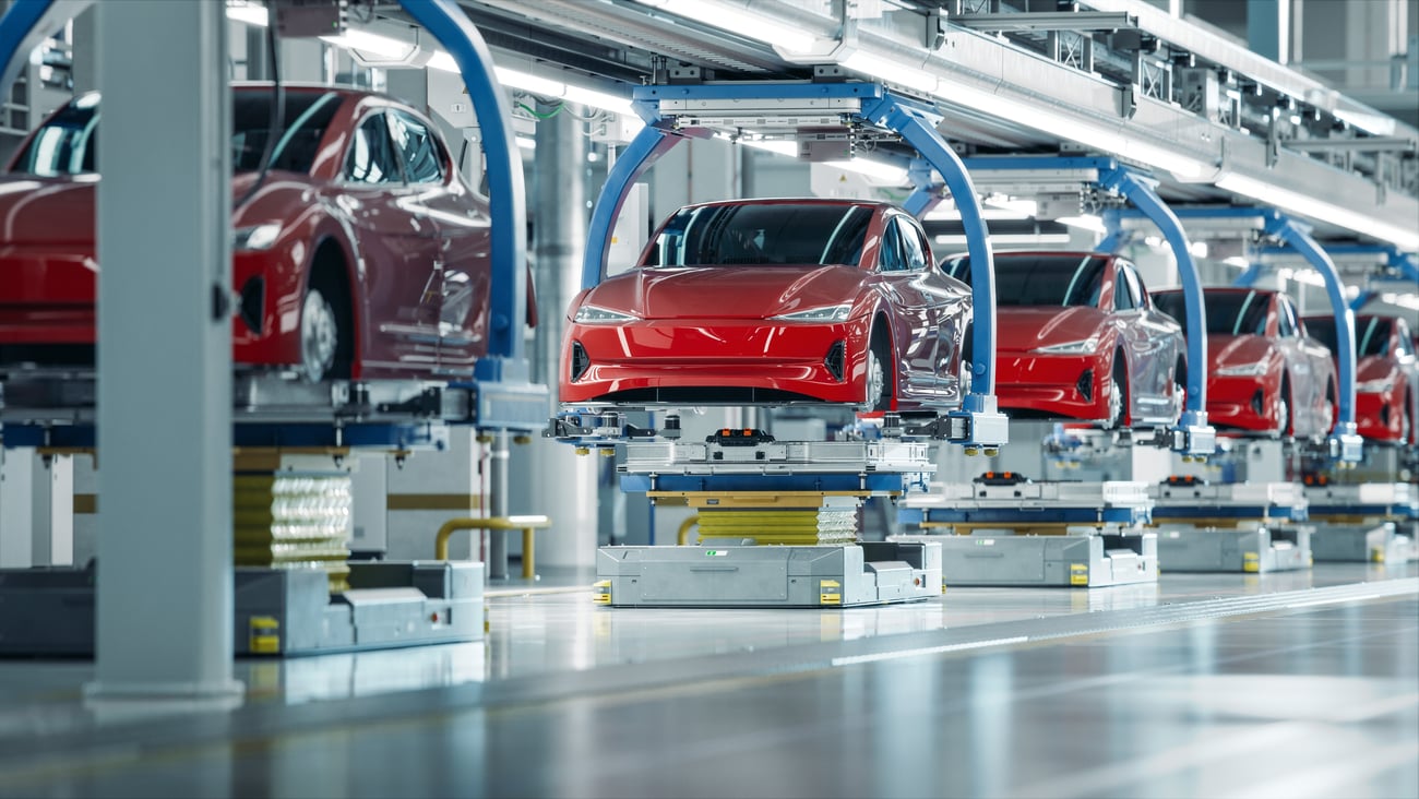 Electric vehicle production, row of red cars hoisted up in factory