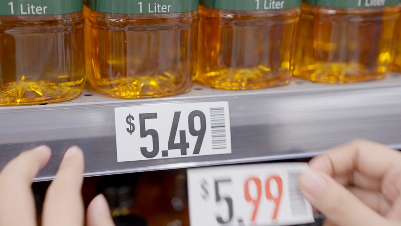 Close up of a shelf with a pricing label for $5.49 being replaced with a tag that reads $5.99
