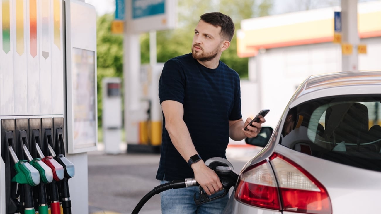 Man filling up his car with gas and staring unhappily at the display on the pumps.