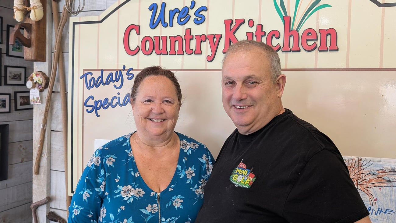 Owners, Laurie and Randy Ure stand in their store, under the shop sign "Ure's Country Kitchen"