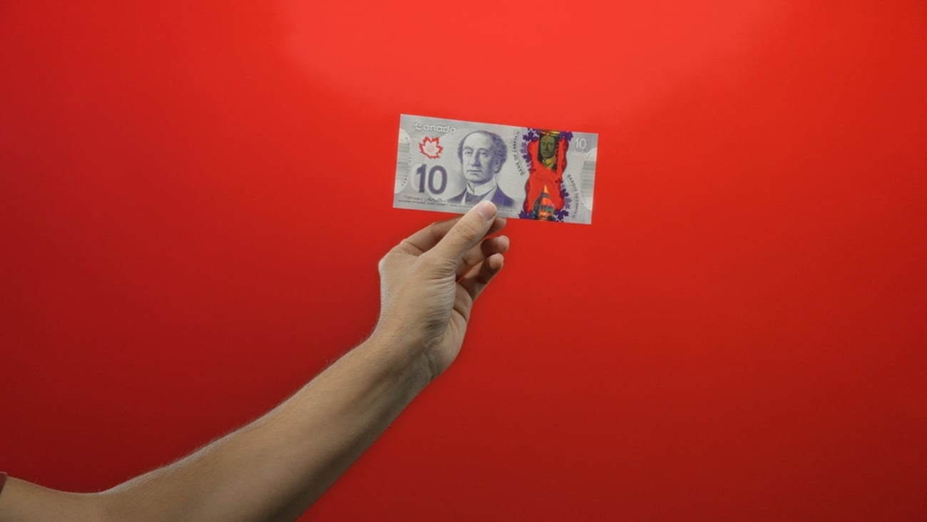 bright red background with a hand holding up a ten dollar Canadian bill.
