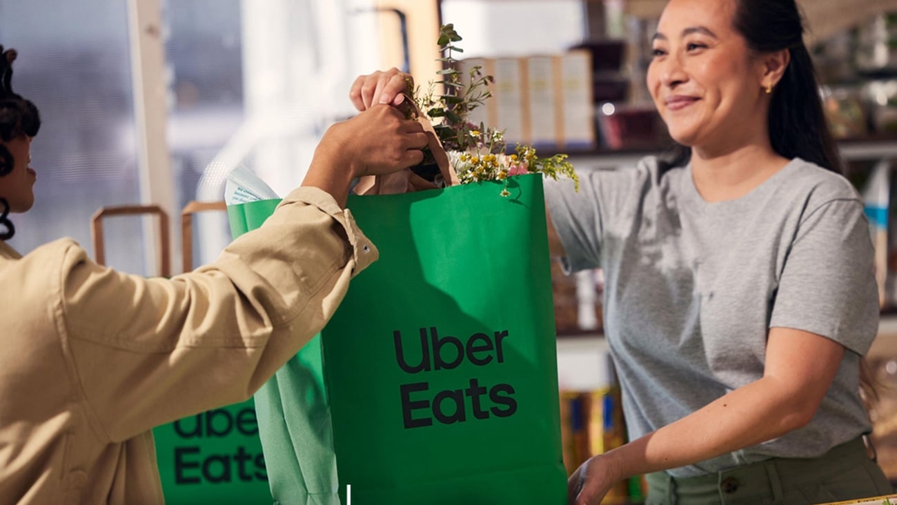 Clerk hands Uber Eats bag to customer