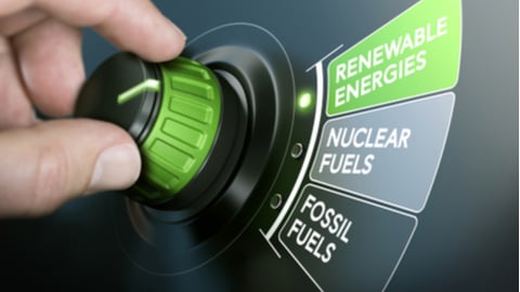 Man turning an energy transition button to switch from fossil fuels to renewable energies. Composite image between a hand photography and a 3D background.