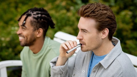 two men on a bench, one is vaping a silver Vuse ePod 2 e-cigarette