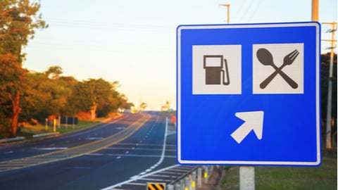 Road sign at the roadside signaling a gas station and food services on highway. Blue board with an arrow informing services straight ahead.