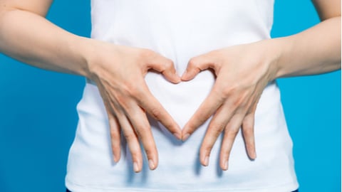 young woman who makes a heart shape by hands on her stomach.