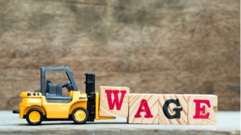 Yellow forklift hold block w to complete word wage on wood background