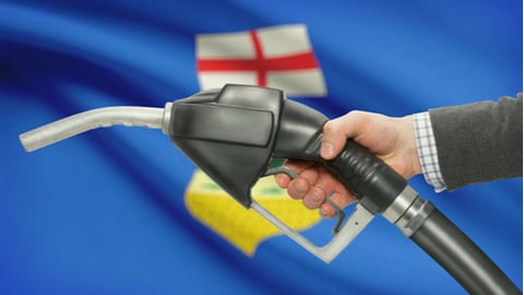 Fuel pump nozzle in hand with Canadian territories and provinces flags on background - Alberta