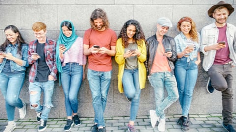 Gen Z group standing against wall using their cell phones