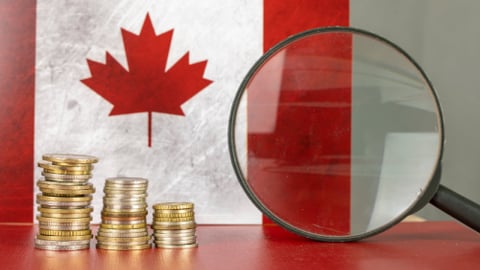 Magnifying glass and coins in front of Canada flag, country economy concept