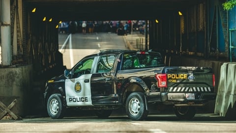 A side closeup of marked Calgary Police Ford F150 blocking traffic at an underpass, people blurred background