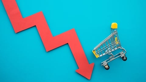 Shopping trolley with red chart falling down on blue background copy space. Global economic recession crisis, core retail sales decrease, inflation or goods price up concept.