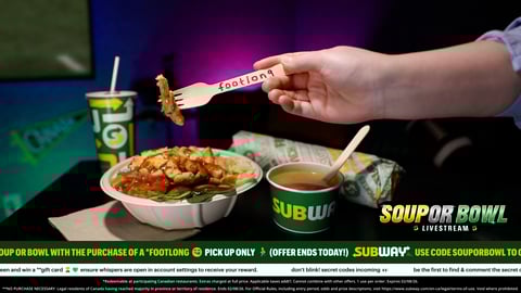 Subway stirfry bowl featured with soup on the side and fork that says "footlong" holding up piece of chicken from the bowl