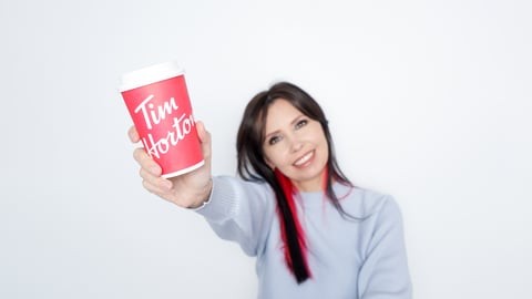 Young white woman with outstretched arm holiding Tim Hortons red coffee cup