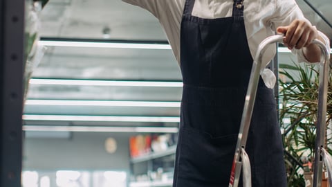 worker in store on a ladder reaching top shelf to get something