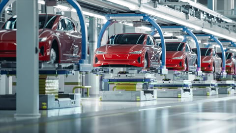 Electric vehicle production, row of red cars hoisted up in factory