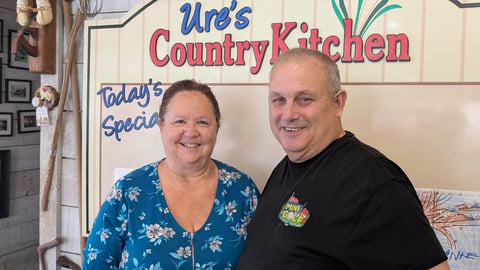 Owners, Laurie and Randy Ure stand in their store, under the shop sign "Ure's Country Kitchen"