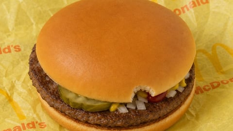A hamburger with a tiny bite taken out of its bun
