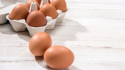 Close-up view of raw chicken eggs in egg box on white wooden background