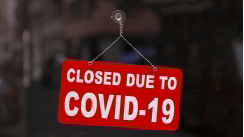 Close-up on a red closed sign in the window of a shop displaying the message "Closed due to Covid-19".