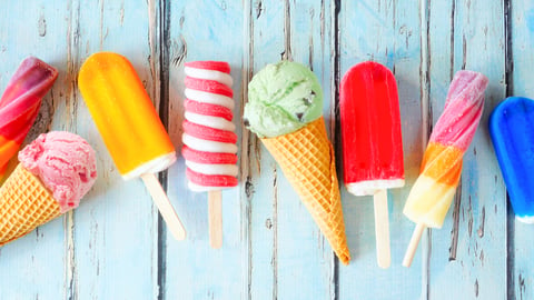 Selection of colorful summer popsicles and ice cream treats. Overhead view scattered on a rustic blue background.