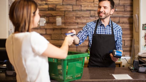 Handsome young man with a beard taking a credit card from a customer at a convenience store