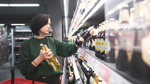 A beautiful girl takes alcoholic drinks from the store shelf. Shopping for alcohol in the store. The girl chooses a drink in the convenience store