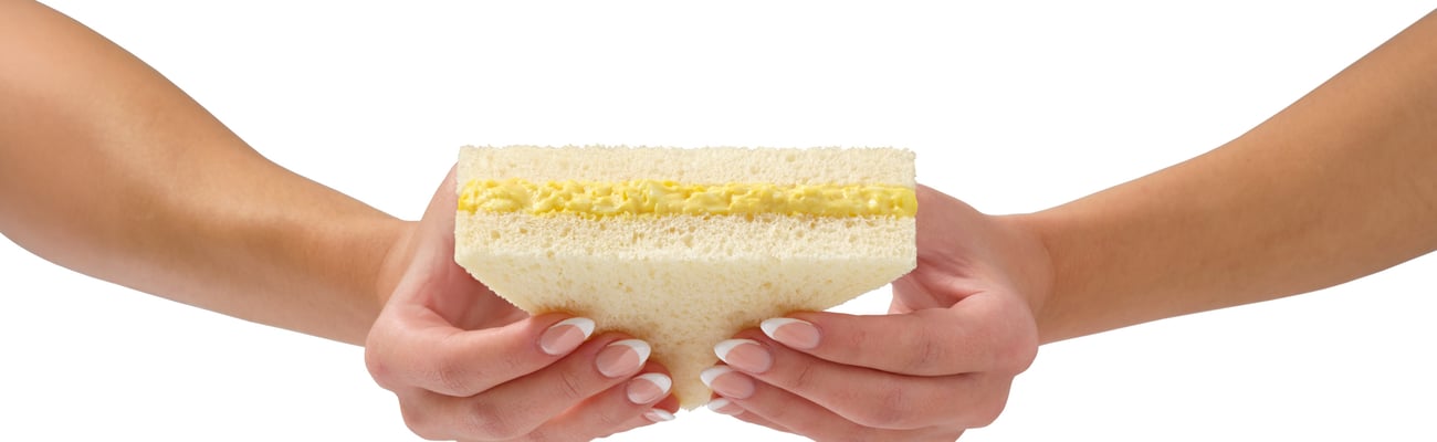 Hands holding egg salad sandwich on white background