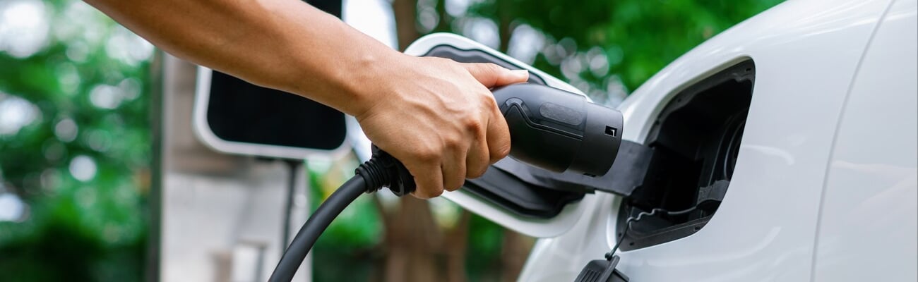 Hand inserting EV charging plug to electric vehicle in focus shot with blurred background of outdoor natural greenery. Progressive sustainable energy powered electric charging station for rechargeable; Shutterstock ID 2307870505