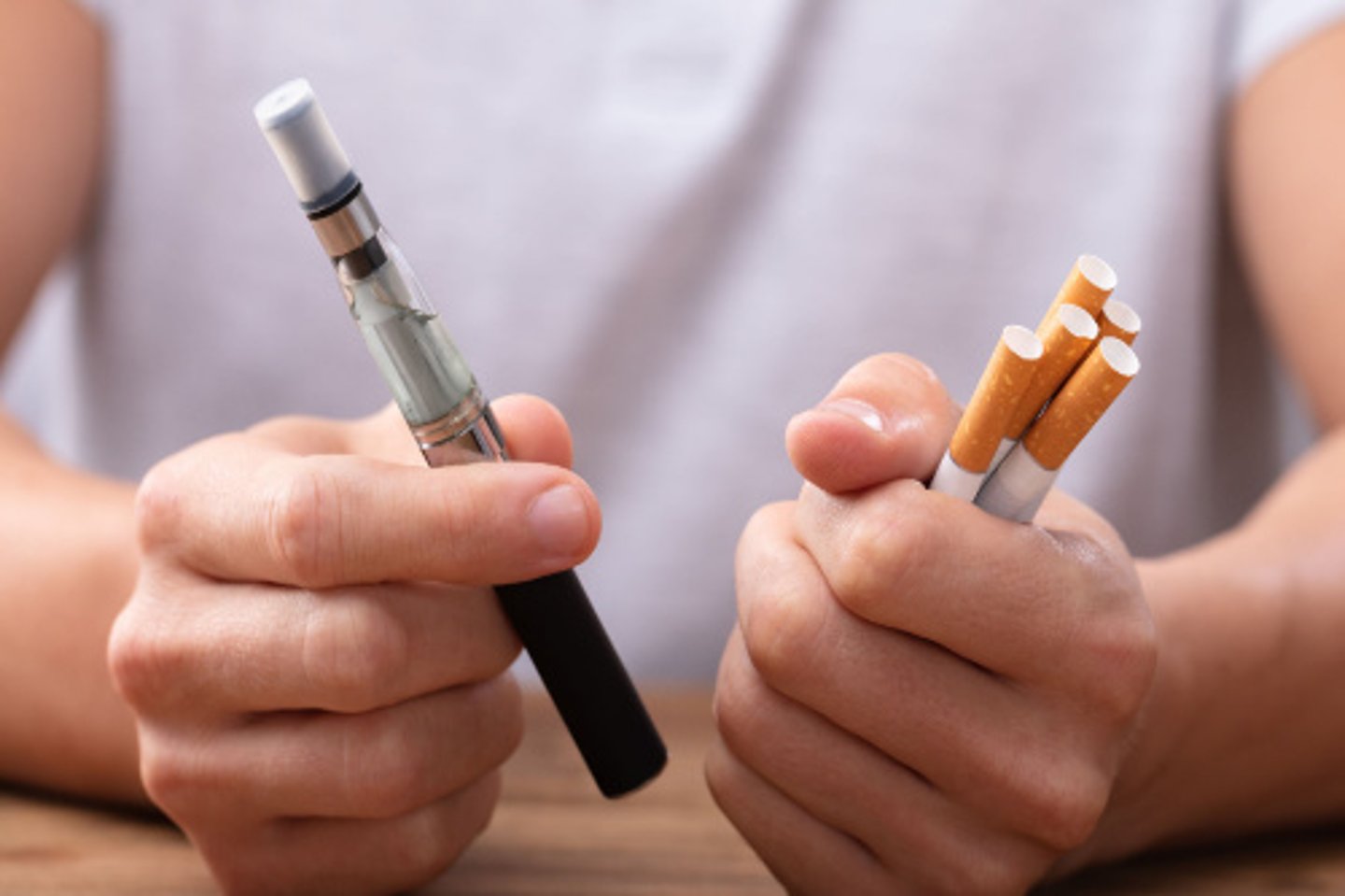 Man Holding Vape And Tobacco Cigarette Over Desk