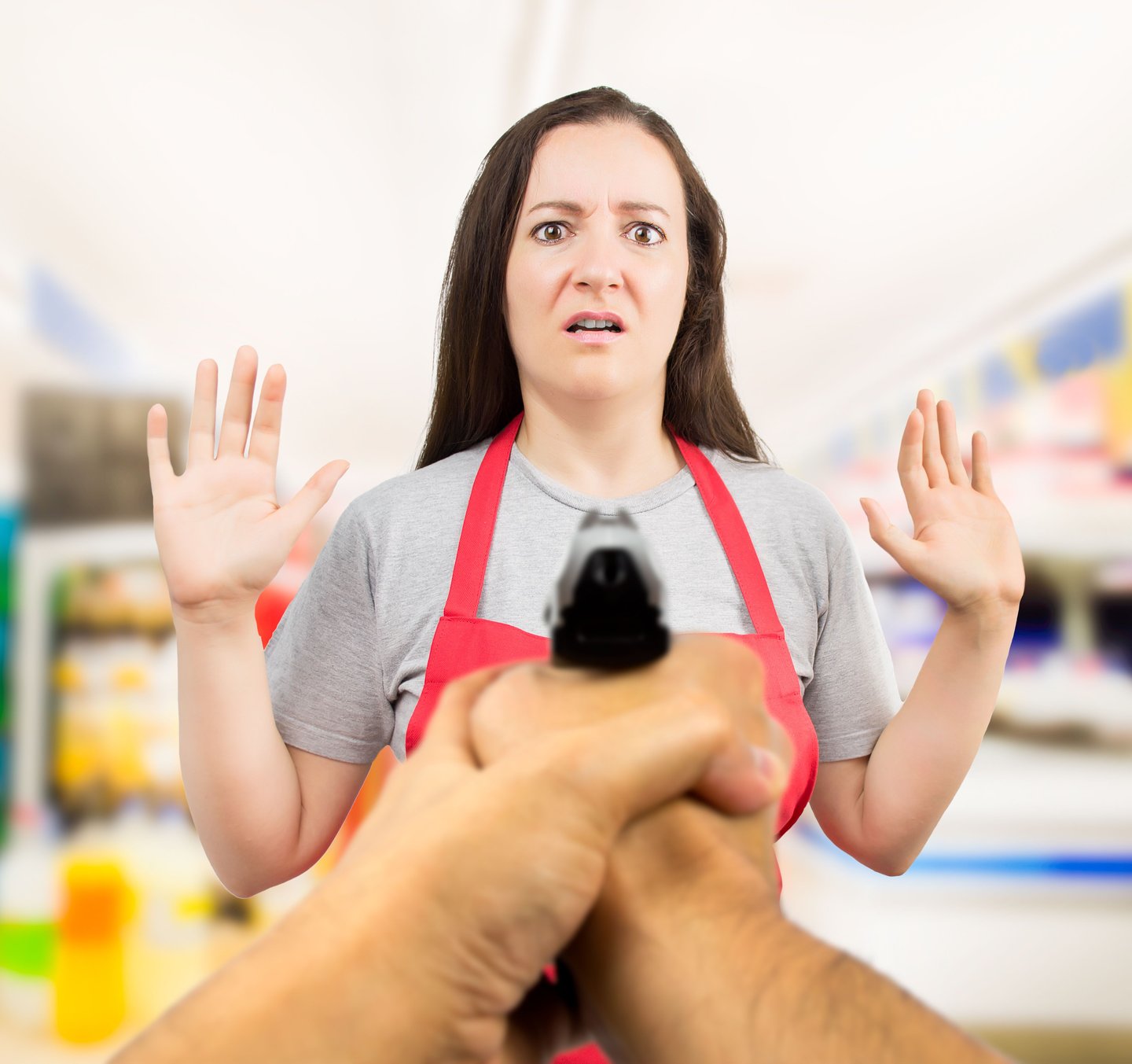 portrait of saleswoman with arms up at the supermarket in a robbery with gun