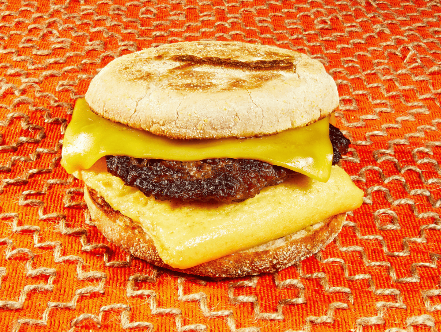 7-Eleven plant-based breakfast sandwich on an English muffin with two cheeses against and orange background. 