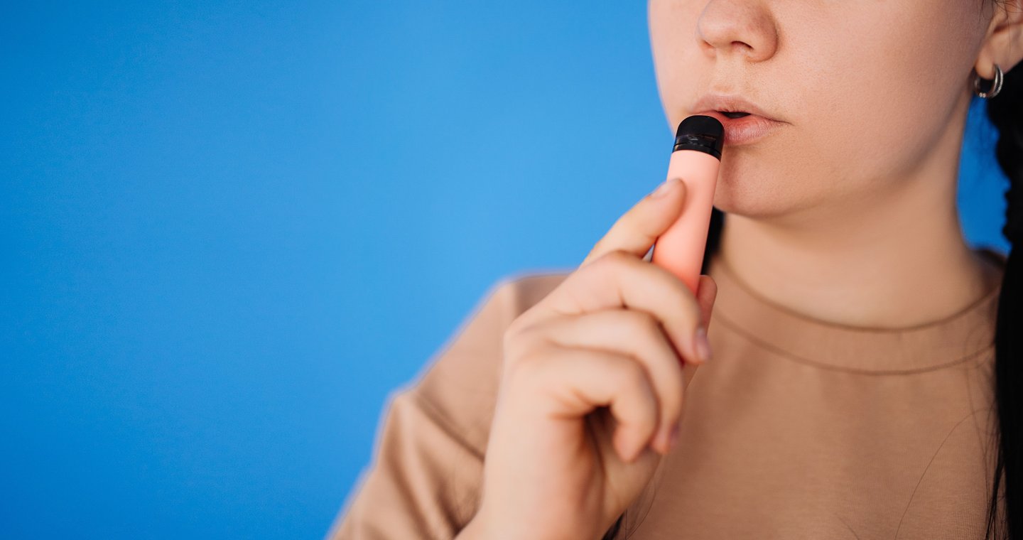  random pretty woman standing and about to hover on a blue background in the studio. the concept of vaping and modern smoking.