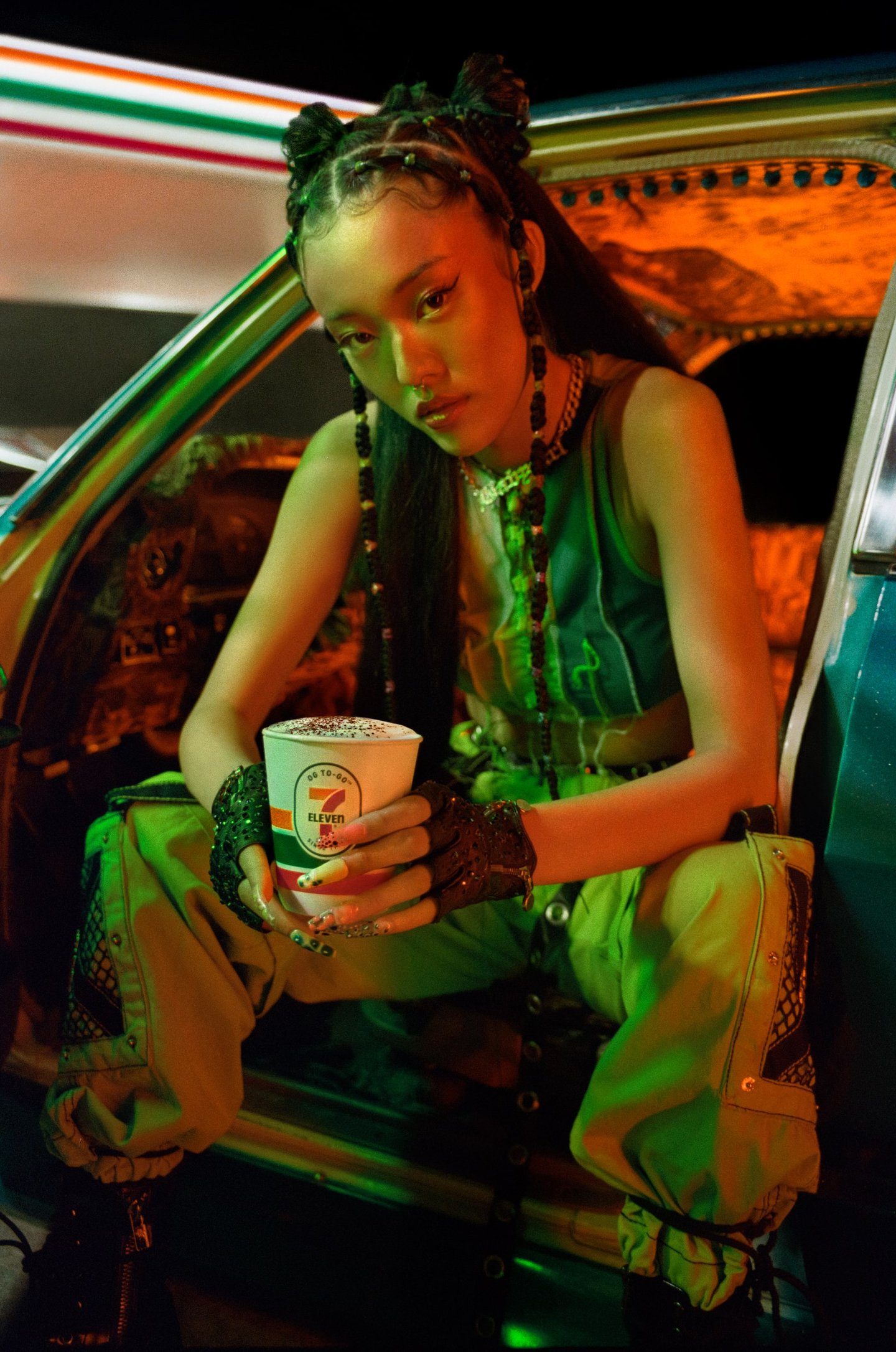 black woman sitting in car at night in front of 7-Eleven drinking coffee