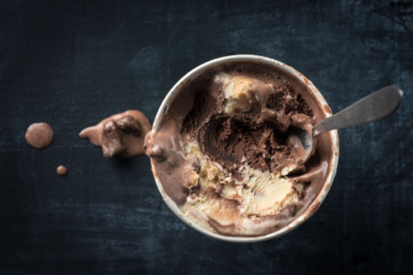 Tub of chocolate ice cream with a spoon in it.