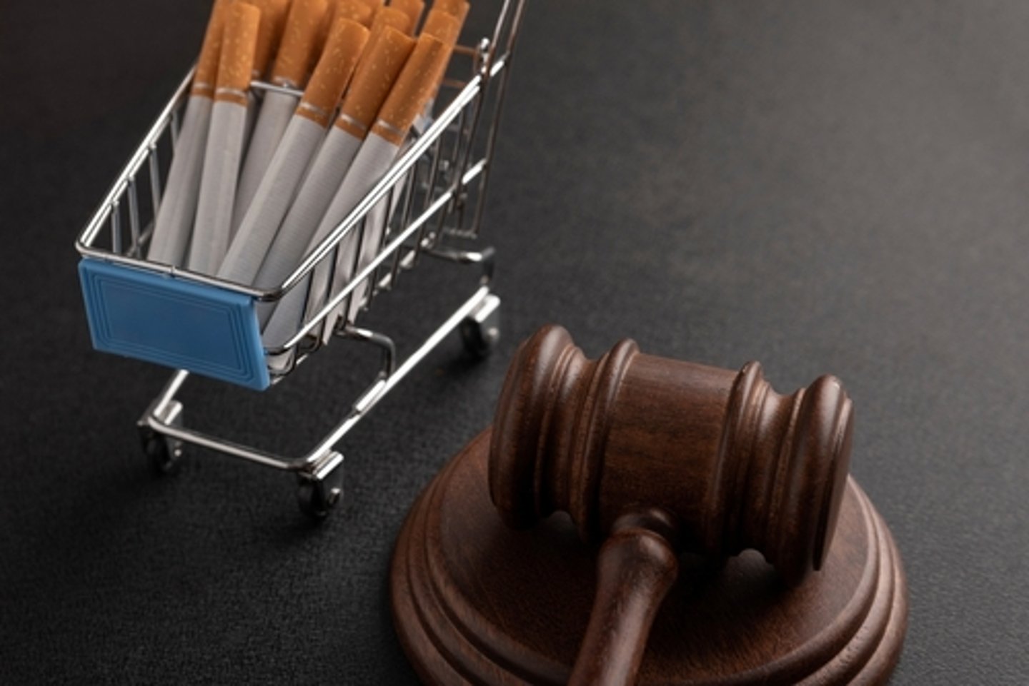 Judge's gavel next to a miniature shopping cart filled with cigarettes