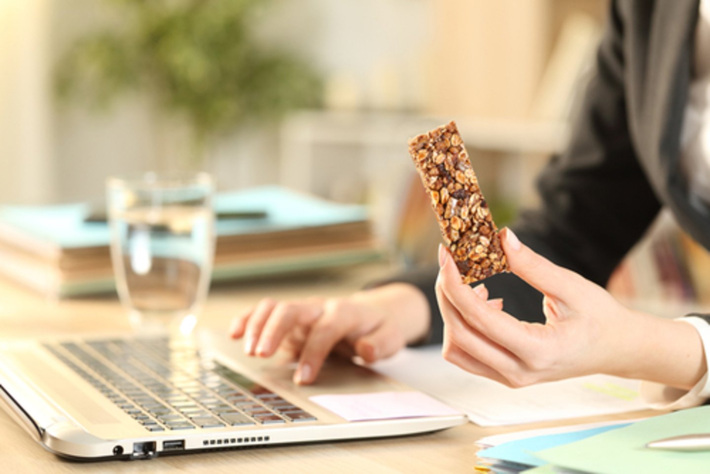 Close up of entrepreneur woman hands holding cereal snack bar working on laptop at home office