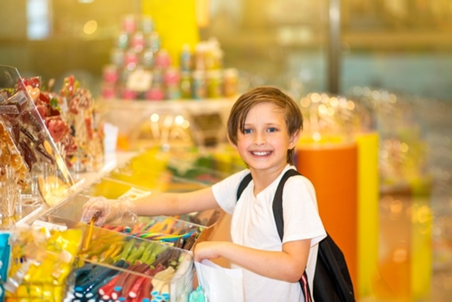 happy little boy in a candy store chooses sweets, marmalade candies, puts them in a paper bag