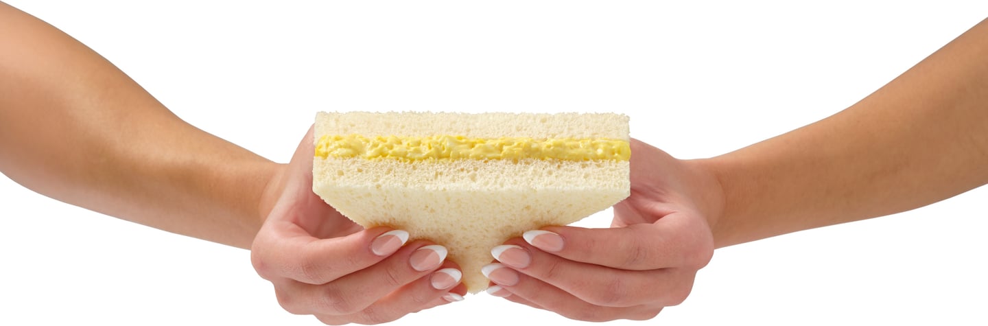 Hands holding egg salad sandwich on white background