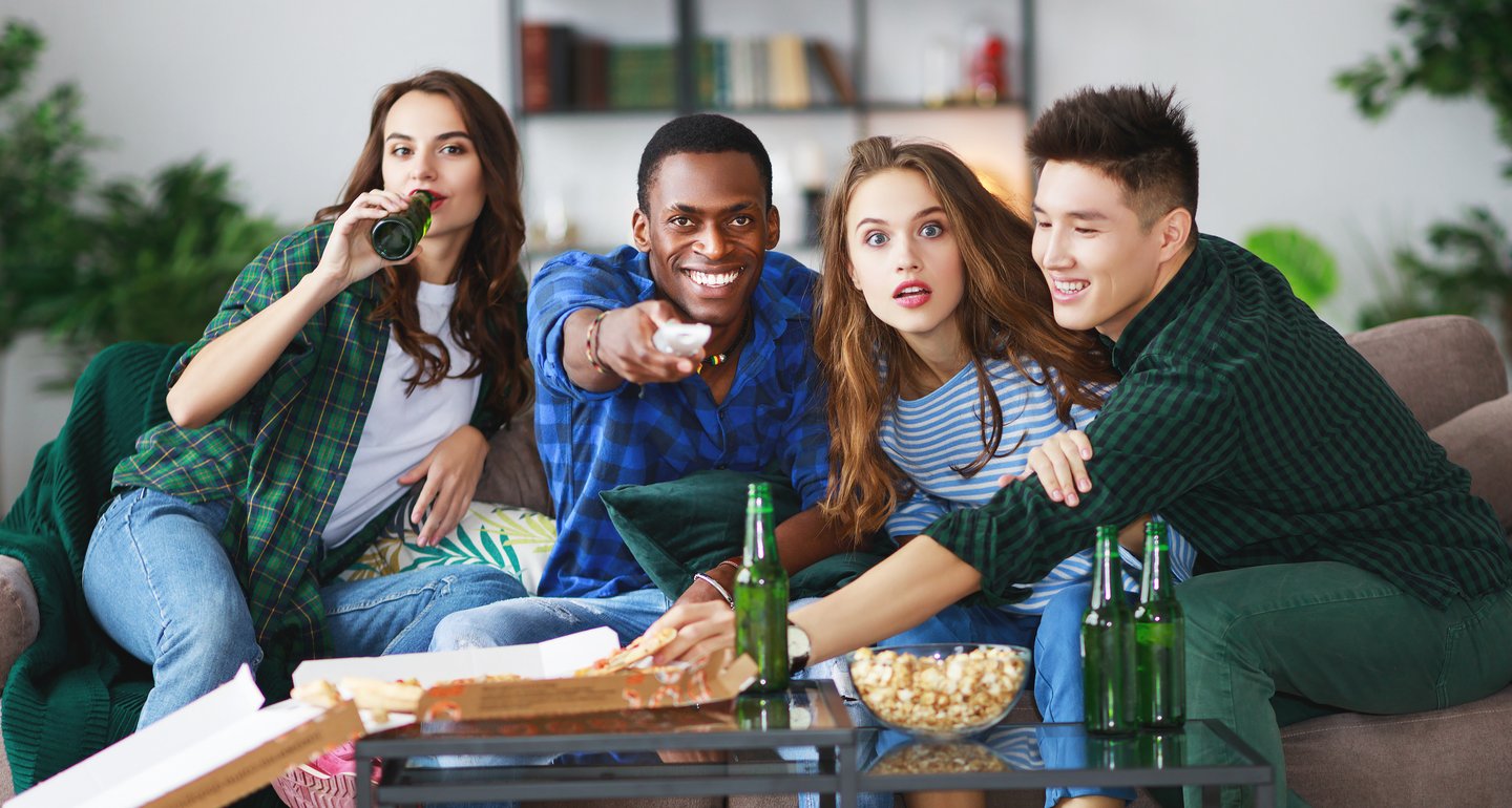 group reacting while watching tv and eating and drinking, at a watch party
