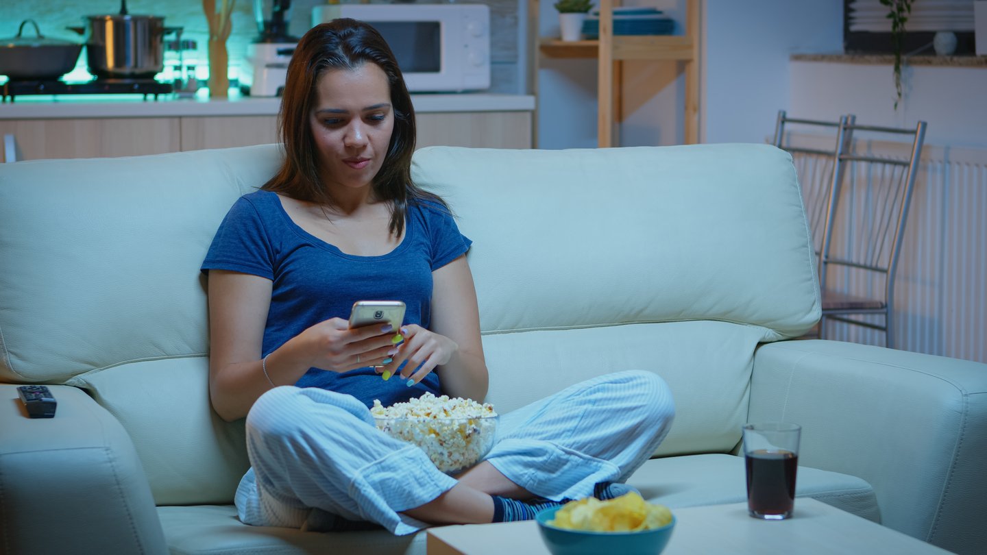 Woman looking at phone and snacking at night