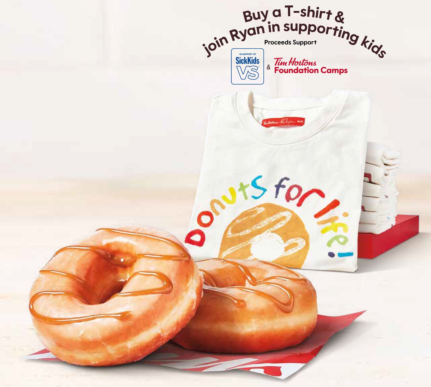 New maple butter glazed doughnut from Tim Hortons, with their fundraising T-shirts for SickKids and Tims Camps in the background.
