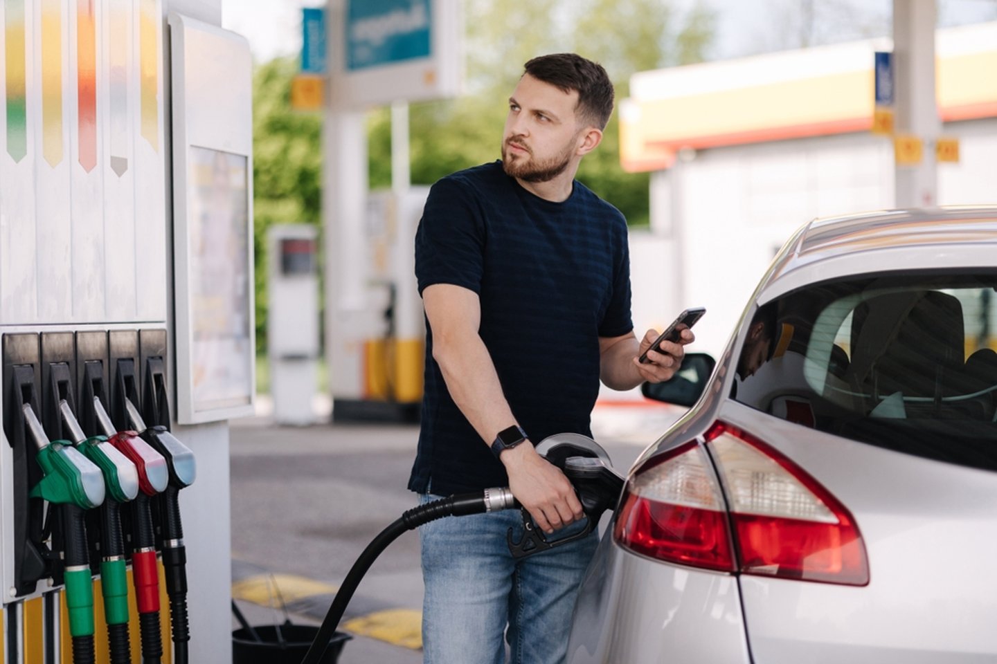 Man filling up his car with gas and staring unhappily at the display on the pumps.