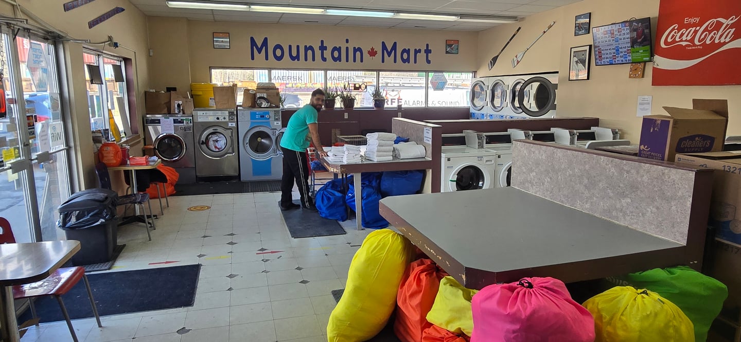 Wide shot of Mountain Mart's laundromat, and someone taking their clothes out of a dryer