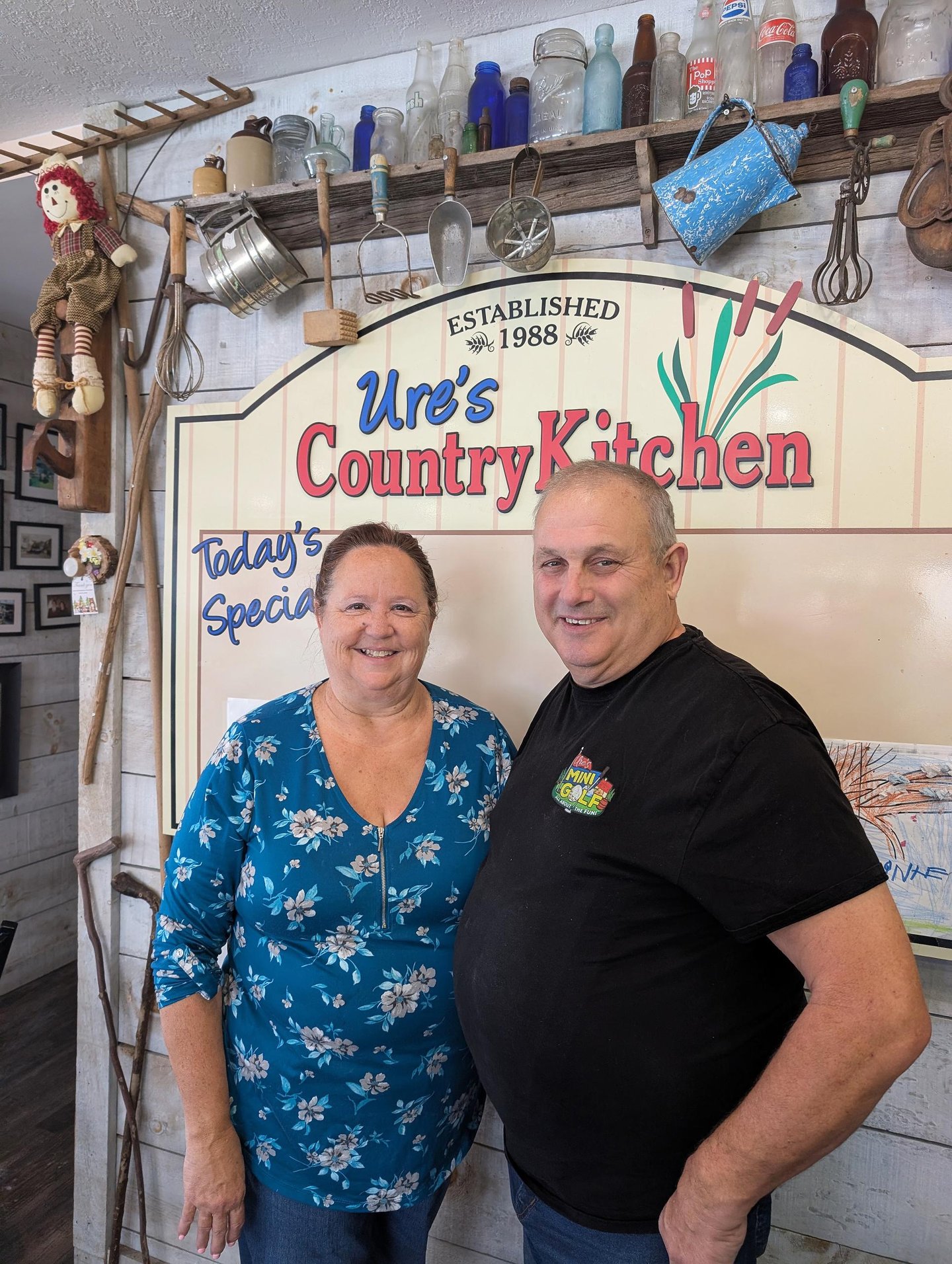 Owners, Laurie and Randy Ure stand in their store, under the shop sign "Ure's Country Kitchen"