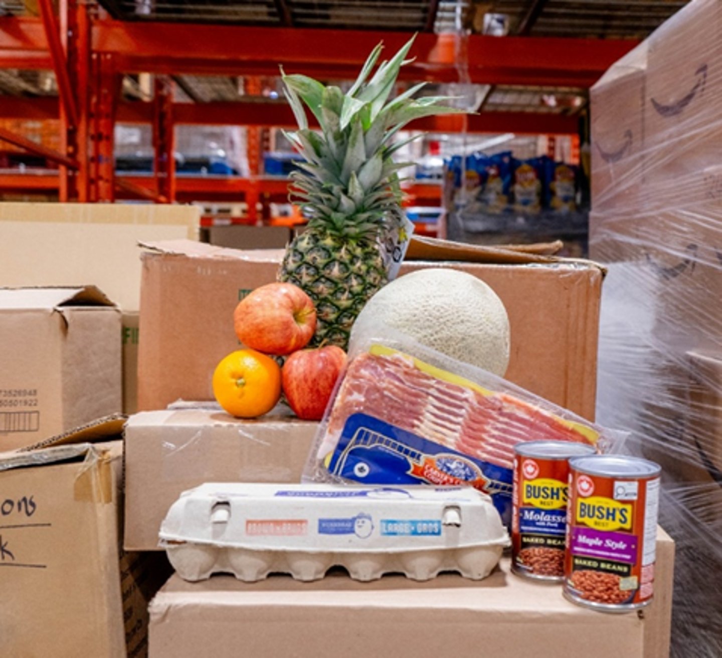 Food donations for Mississauga food bank: Pineapple, eggs, bacon and can of beans on top of cardboard boxes.