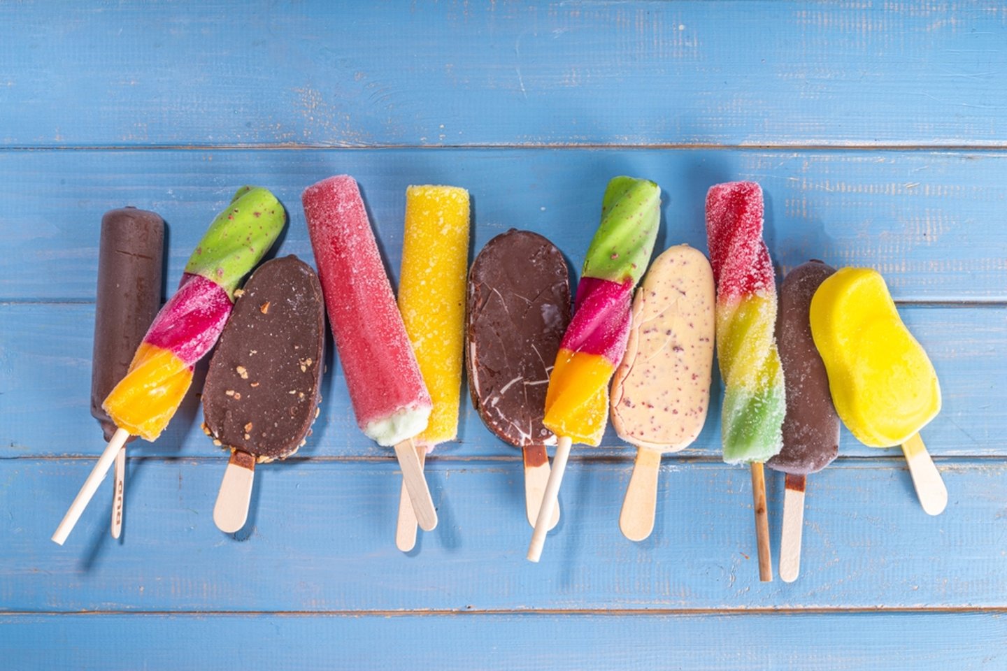 Assorted popsicles and chocolate-covered ice cream on a stick, on a blue painted wooden background 