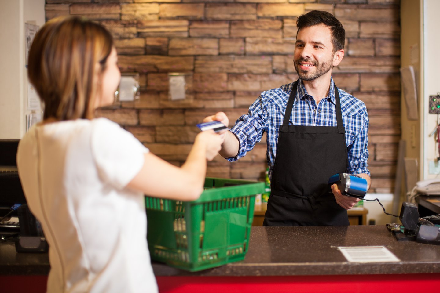 Handsome young man with a beard taking a credit card from a customer at a convenience store